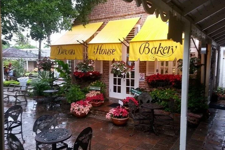 Außenansicht der Devon House Bakery mit gelben Markisen und Sitzgelegenheiten im Freien.