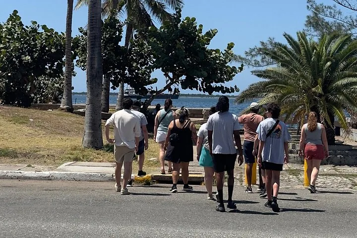 Menschengruppe geht in Richtung Wasser, im Hintergrund ein Schiff.